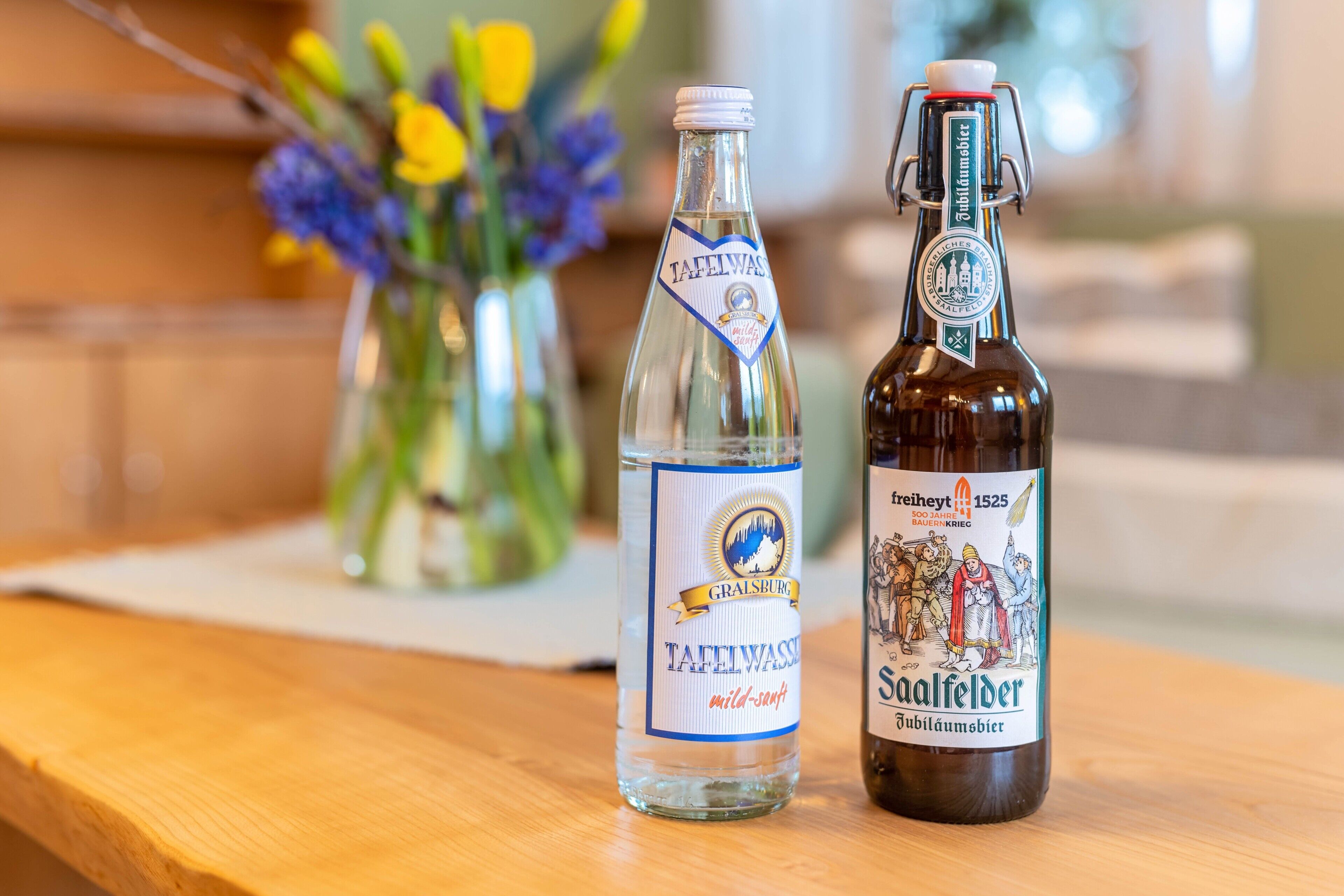 Two bottles of beer on a wooden surface with a blurred background of a room.