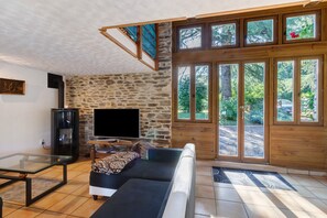 A living room with a stone wall, a sofa, a glass coffee table, a TV, and a wooden staircase. - Charming Cottage in the Périgord Vert Countryside (Angoisse)
