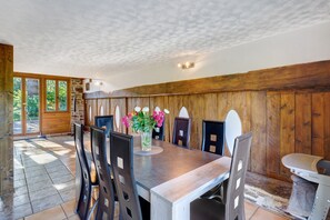 A dining area with a wooden table, chairs, a vase with flowers, and a view of greenery outside. - Charming Cottage in the Périgord Vert Countryside (Angoisse)