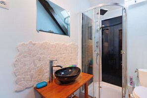 A bathroom with a stone wall, a wooden vanity, a black vessel sink, a glass shower enclosure, and a toilet. - Charming Cottage in the Périgord Vert Countryside (Angoisse)