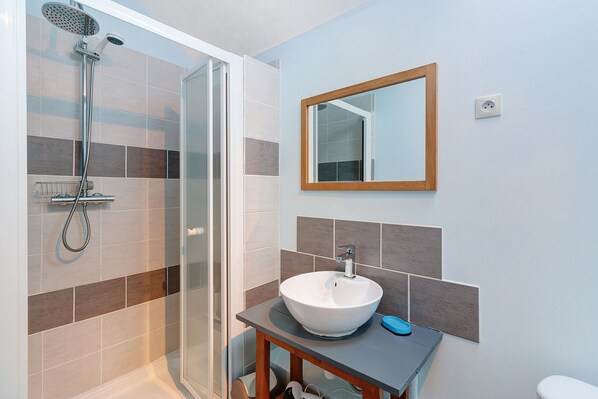 A bathroom with a glass shower enclosure, a white sink, and a mirror on the wall. - Charming Cottage in the Périgord Vert Countryside (Angoisse)