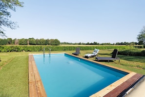 A rectangular swimming pool with a wooden deck, two lounge chairs, and a metal ladder.