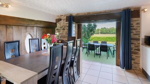 An indoor dining area with a stone wall, wooden ceiling, and a view of a garden through a glass door. - Charming Cottage in the Périgord Vert Countryside (Angoisse)