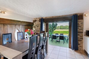 An indoor dining area with a stone wall, wooden ceiling, and a view of a garden through a glass door. - Charming Cottage in the Périgord Vert Countryside (Angoisse)