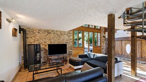 A living room with a stone wall, a TV, a sofa, and a staircase. - Charming Cottage in the Périgord Vert Countryside (Angoisse)