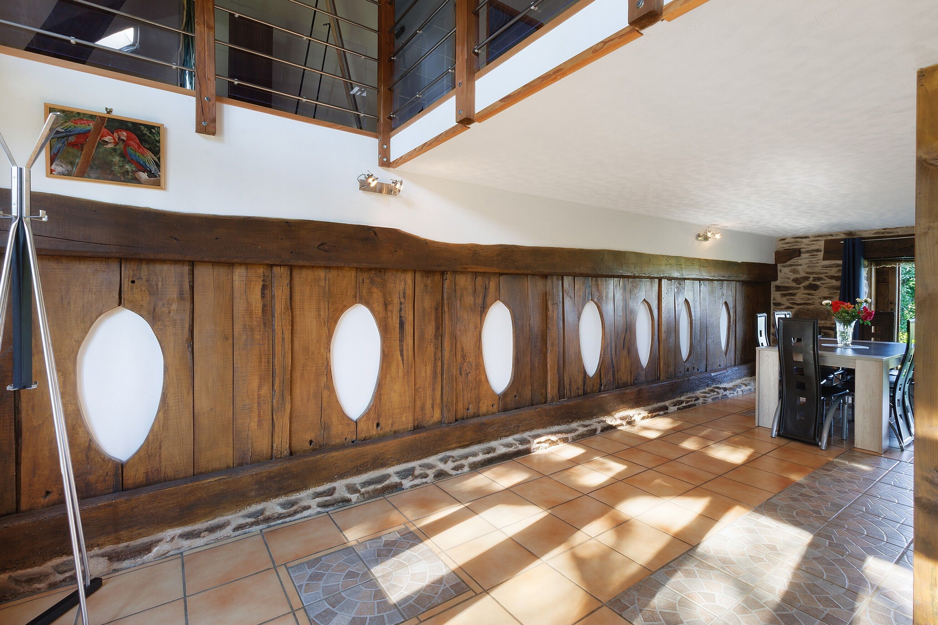 Una habitación amplia con techo alto, paneles de madera, un muro decorativo de piedra y un comedor con mesa y sillas.