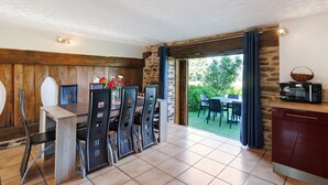 A dining area with a wooden table and chairs, a stone wall, and a view of the outdoors. - Charming Cottage in the Périgord Vert Countryside (Angoisse)