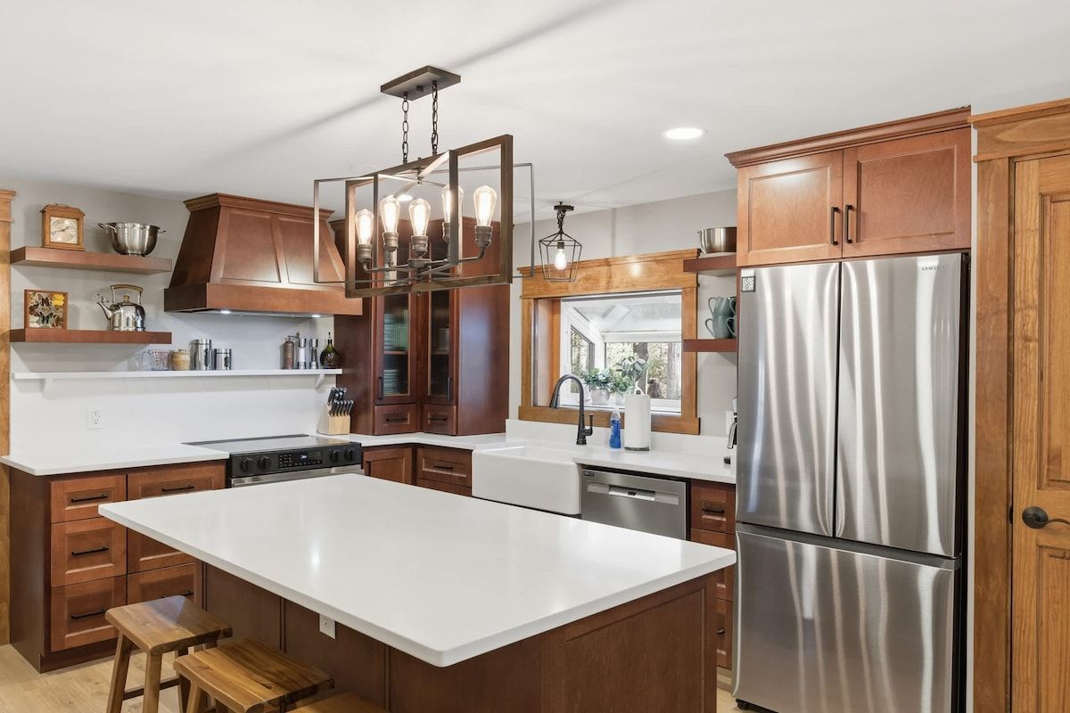 A modern kitchen with a large island, stainless steel appliances, wooden cabinetry, and pendant lighting.