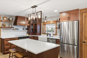 A modern kitchen with a large island, stainless steel appliances, wooden cabinetry, and pendant lighting. - NEW Cabin on 3 Acres  W/ Hot Tub+Sauna - Sleeps 8 (Travelers Rest)