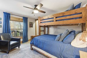 Un lit superposé avec un ventilateur de plafond, une chaise et une fenêtre avec des rideaux.