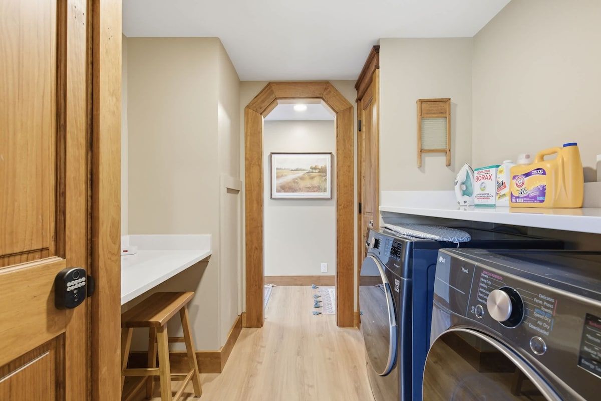 A laundry room with a washing machine, a wooden door, a bench, and a small table.