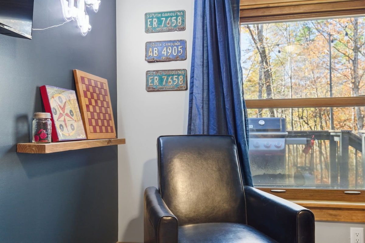 A room with a black leather chair, a window with a view of trees, and three South Carolina license plates on the wall.