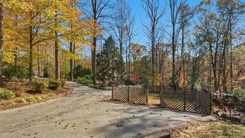 A paved driveway leading into a wooded area with a fence and a gate.