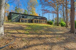 A modern house with a deck, surrounded by trees and a grassy area.