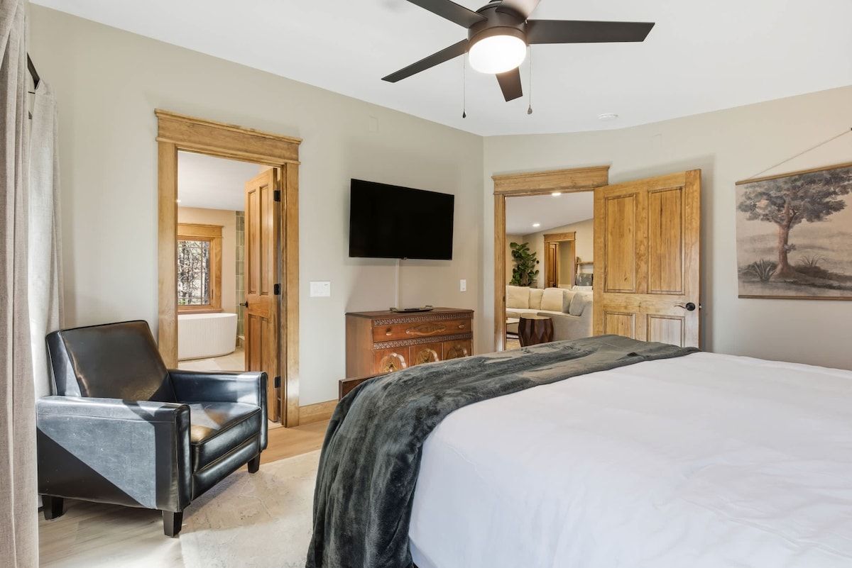 A bedroom with a bed, a chair, a television, and a ceiling fan.
