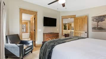 A bedroom with a bed, a chair, a television, and a ceiling fan.