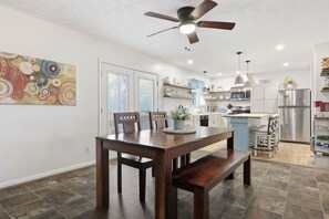 Una cocina moderna con armarios blancos, un refrigerador de acero inoxidable y un comedor con mesa y sillas de madera.