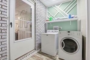 Un lavadero con lavadora y secadora, una pared de ladrillo y una puerta que da a otra habitación.