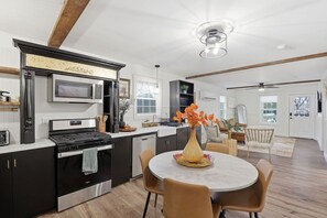 Una cocina moderna con microondas, estufa y lavavajillas integrados. Hay una zona de comedor con una mesa redonda y sillas, y un florero con flores sobre la mesa.