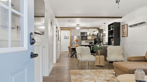 A modern living room with a sofa, chairs, and a coffee table. There is a dining area with a table and chairs. The room has a wooden floor and white walls.