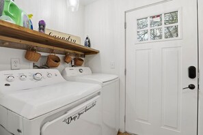 A laundry area with two washing machines, a drying rack, and a shelf with laundry supplies. - Cute Cottage, Central Location, Pet Friendly (Greer)