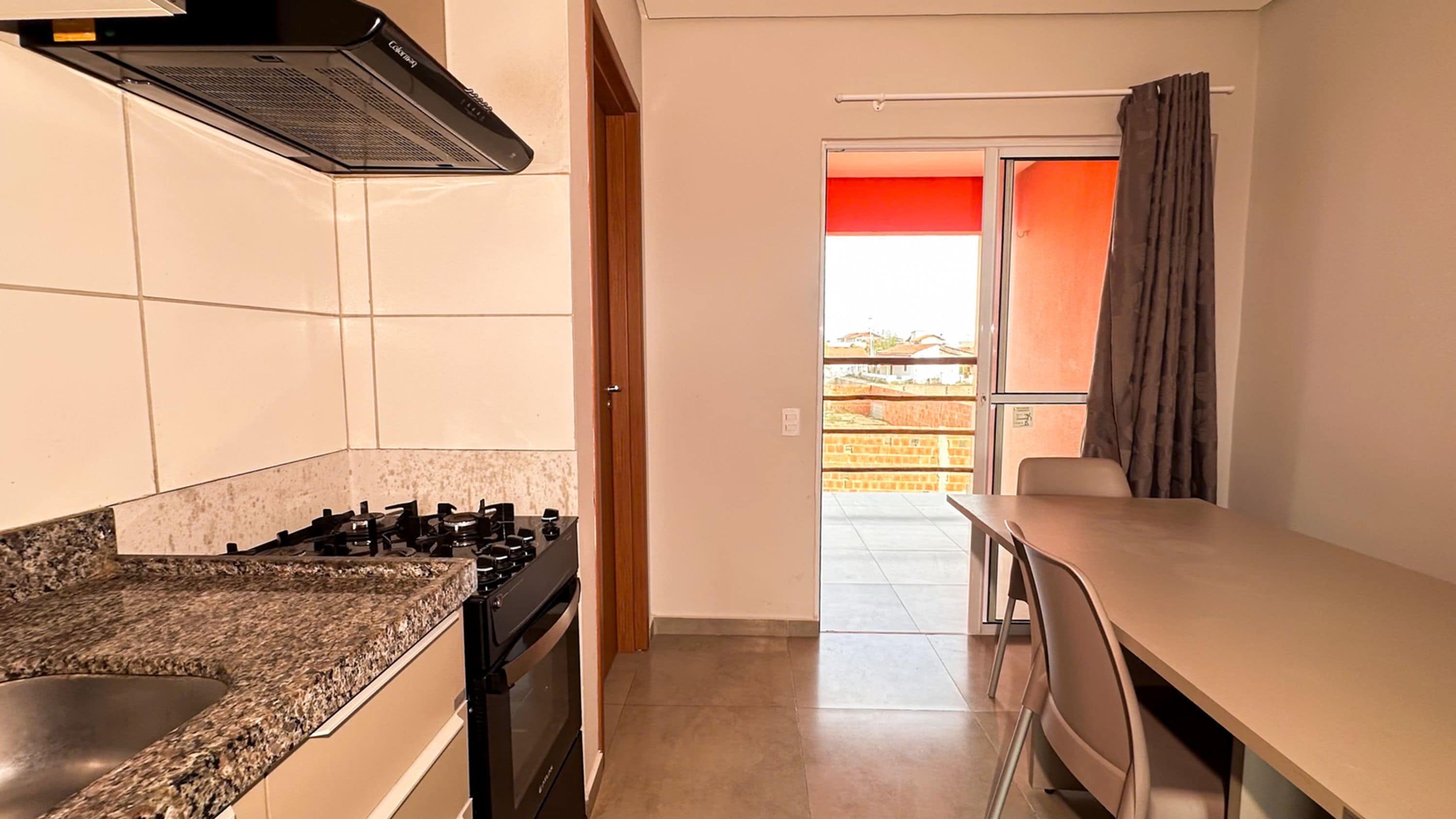 Une cuisine compacte équipée d’une cuisinière à gaz, d’un four encastré et d’un four à micro-ondes. Un coin repas avec une table et des chaises est également disponible. Une porte coulissante donne accès à un balcon offrant une vue sur les environs.