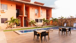 A hotel with a swimming pool, outdoor seating, and a staircase leading to the building. - Apto com Wi Fi Garagem e Piscina a 100m da Praia (Luis Correia)