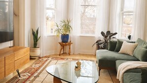 A living room with a green sofa, a coffee table, a TV, and several potted plants. - Logan Sq 4BR Duplex • Garage • Sleeps 8 (Chicago)