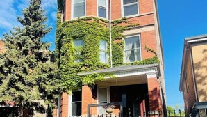 A two-story brick building with a prominent corner entrance, a gated driveway, and a large tree in front. - Logan Sq 4BR Duplex • Garage • Sleeps 8 (Chicago)