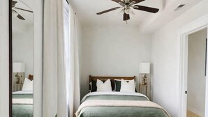 A bedroom with a bed, ceiling fan, bedside lamps, and a large mirror. - Logan Sq 4BR Duplex • Garage • Sleeps 8 (Chicago)