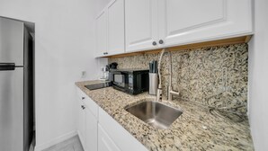 Una cocina con armarios blancos, encimera de granito, pileta de acero inoxidable, microondas y refrigerador.
