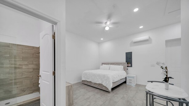 Un dormitorio moderno con cama, mesita de noche, una silla y una pequeña mesa con un jarrón.