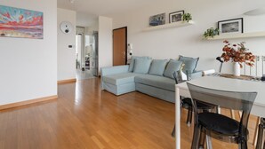 Un salon moderne avec un canapé d’angle, une table à manger avec des chaises, et une cuisine en arrière-plan.