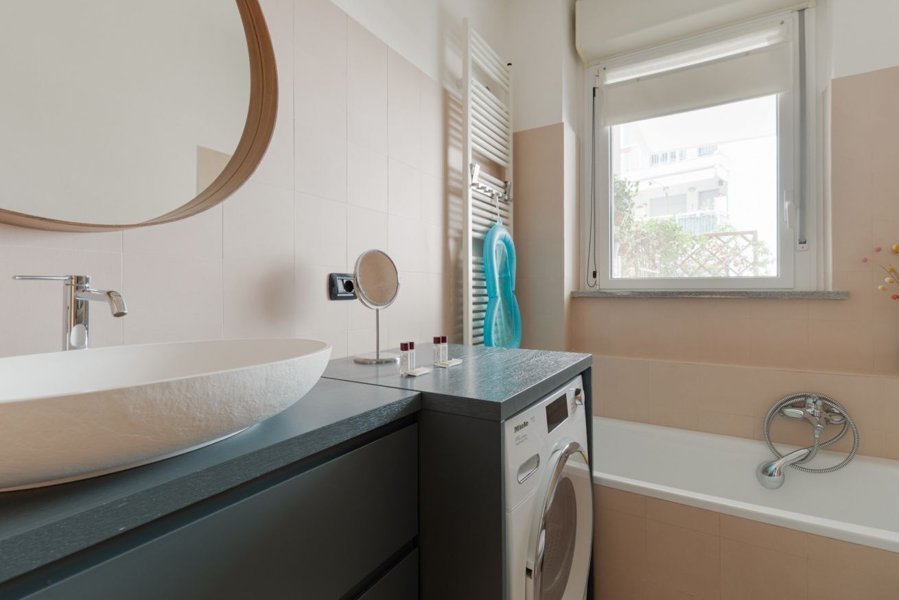 Ein Badezimmer mit einem großen Waschbecken, einem Spiegel, einer Waschmaschine und einer Badewanne.