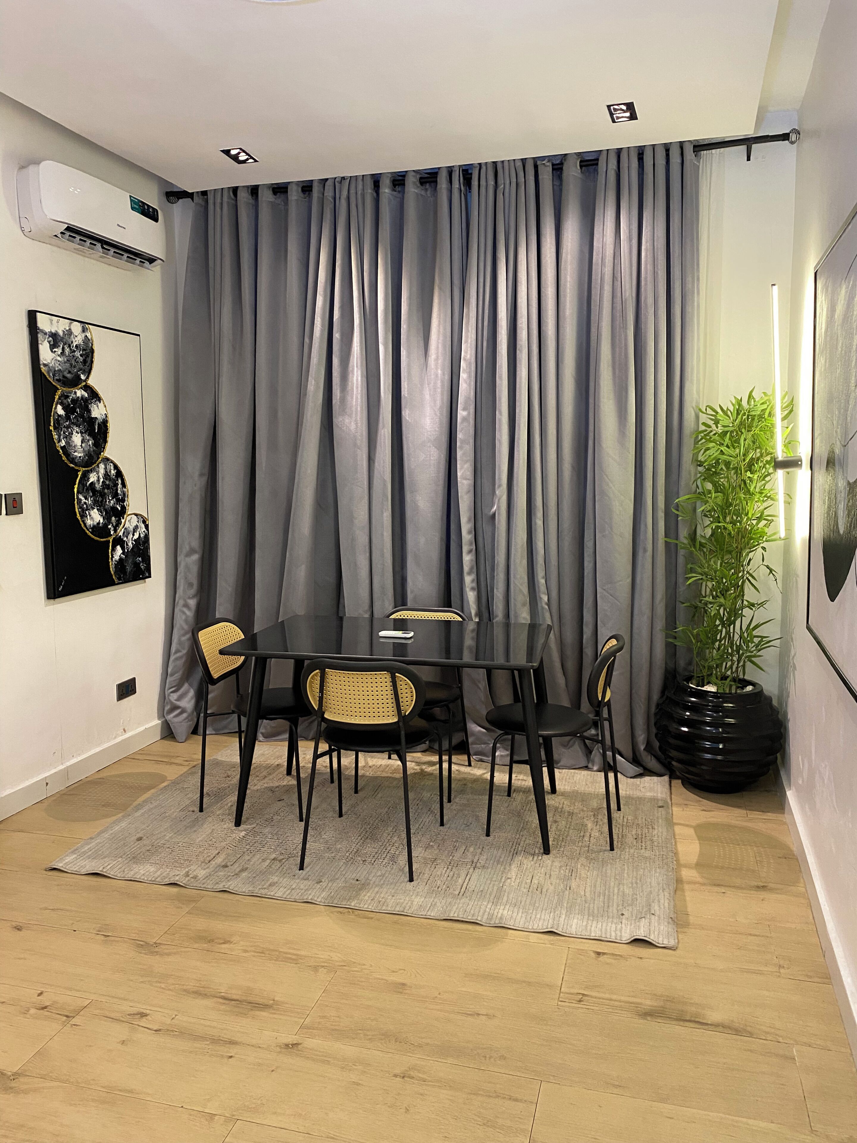 A dining area with a table and chairs, a grey curtain, a potted plant, and a wall-mounted air conditioner.