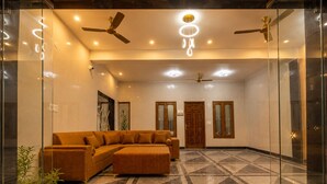 A spacious lobby with a large sectional sofa, ceiling fans, recessed lighting, and a patterned floor. - Tamarind Leaf Residency Noida Sector 50 Metro & Spectrum Mall (Noida)