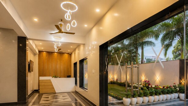 A modern hotel lobby with a reception desk, a ceiling fan, and a glass entrance leading to a garden with potted plants. - Tamarind Leaf Residency Noida Sector 50 Metro & Spectrum Mall (Noida)