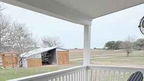 A covered porch with a wooden table and two Adirondack chairs. - Private Hilltop Estate Near Round Top - Main House, Guest House & Barn (Fayetteville)