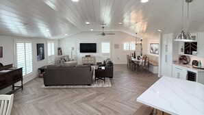 A spacious living area with a herringbone floor pattern, a large sofa, a dining table, and a kitchen area with white cabinets and a marble countertop. - Private Hilltop Estate Near Round Top - Main House, Guest House & Barn (Fayetteville)