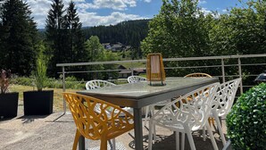 An outdoor patio with a table and chairs, surrounded by greenery and a scenic view of houses and trees. - Bavaria Mountain Ski Lodge Dog Pool terrace grill (Lohberg)