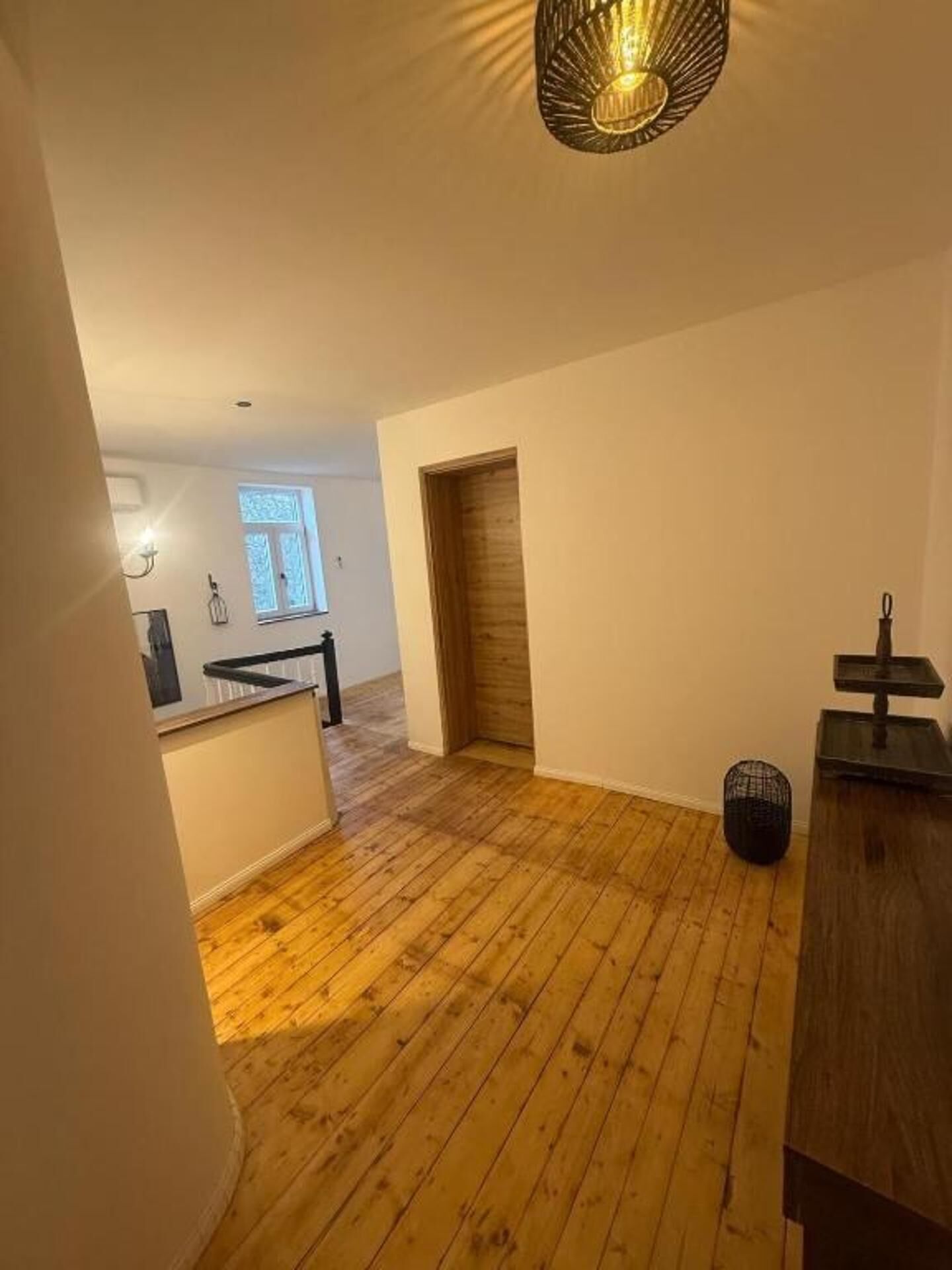A spacious room with wooden flooring, a small kitchen area, and a wooden door.