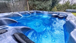 Un jacuzzi con interior azul transparente, rodeado por un muro de piedra y follaje.