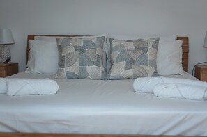 Un lit bien fait, avec une tête de lit en bois, du linge de lit blanc et des coussins à motifs.