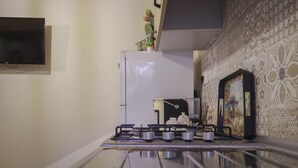 A kitchen with a gas stove, a refrigerator, and patterned tiles on the wall. - Vacation home La Ficurinia in the heart of the historic center of Syracuse (Siracusa)