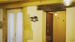 A room with a wooden ceiling, a white door with a curtain, a wall-mounted shelf with bottles, and a light fixture. - Vacation home La Ficurinia in the heart of the historic center of Syracuse (Siracusa)