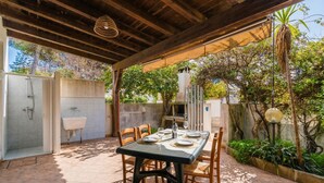Una terrazza esterna con tavolo apparecchiato per mangiare, zona doccia coperta e giardino con piante e una palma.