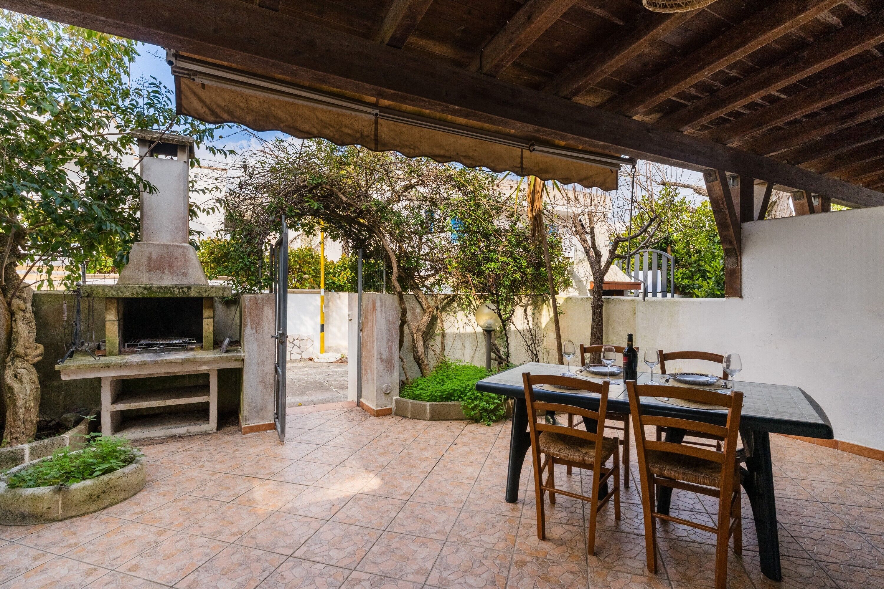 An outdoor patio with a grill, dining table, chairs, and a pergola structure.