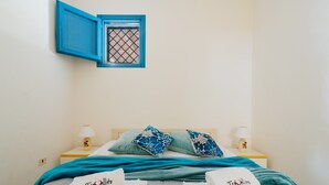 Un letto rifatto con cura, decorato in bianco e blu, due abat-jour e una piccola finestra con cornice azzurra.