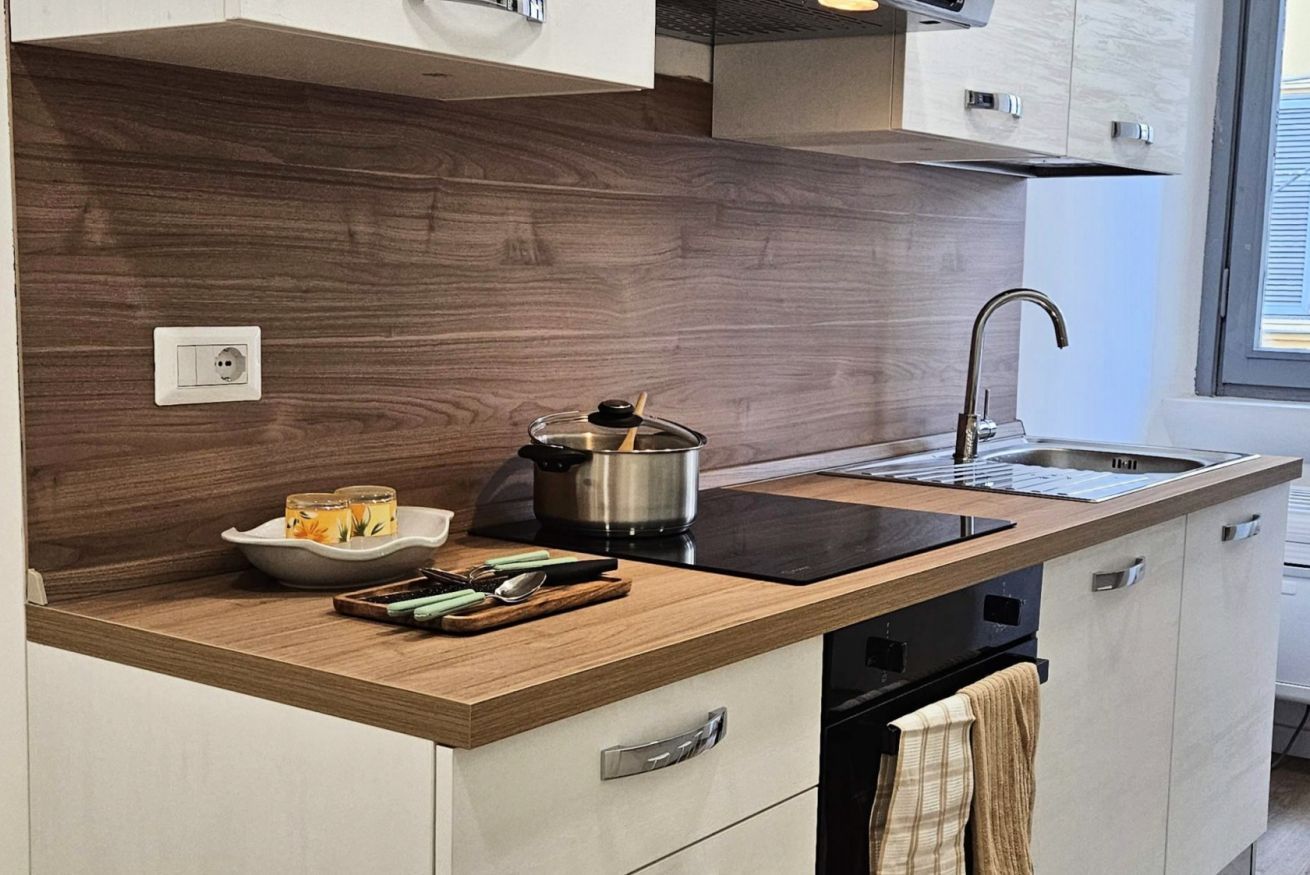 Une cuisine moderne avec un revêtement mural en bois, une plaque de cuisson à induction noire, un évier en acier inoxydable et un four encastré.