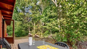 Una terraza de madera al aire libre con una mesa dispuesta para comer, rodeada de abundante vegetación y árboles.